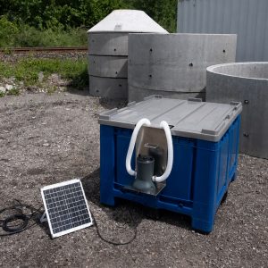 Blaue Bigbox mit grauem Deckel, Solarpanel und integrierter Pumpe zur autarken Wasseraufbereitung auf einem Außengelände.