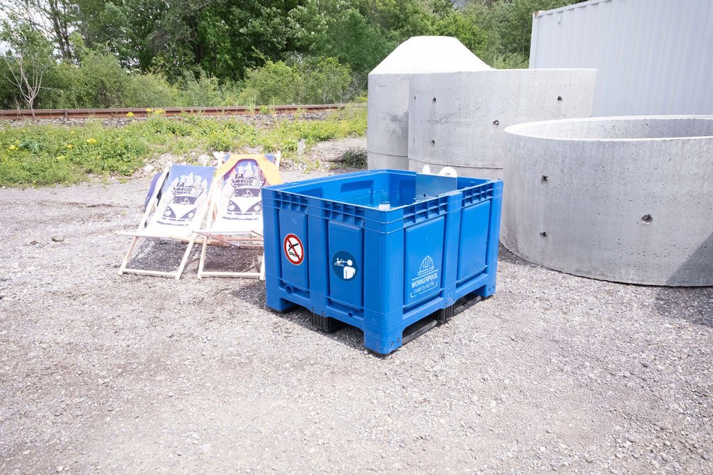 Blaue Bigbox des Workerpools im Außenbereich auf Schotterfläche mit weißem Logo und Sicherheitsaufklebern