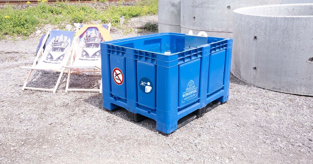 Blaue Bigbox des Workerpools im Außenbereich auf Schotterfläche mit weißem Logo und Sicherheitsaufklebern