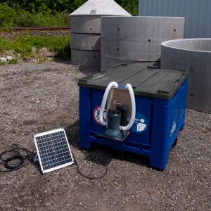 Blaue Bigbox mit grauem Deckel, Solarpanel und integrierter Pumpe zur autarken Wasseraufbereitung auf einem Außengelände.