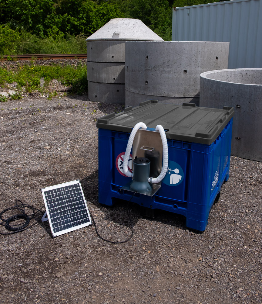 Blaue Bigbox mit grauem Deckel, Solarpanel und integrierter Pumpe zur autarken Wasseraufbereitung auf einem Außengelände.